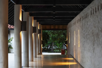 Interior perspective space of passageway on long open end corridor to the outdoor garden with repeated concrete column and old textured wall decorated by light for travel background.