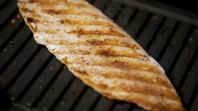 Close up video of seasoned hake fillet cooking on a grill. Grilled fish.