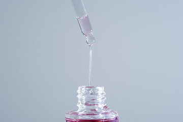 Pink face oil drop from glass pipette dropper. Macro close up for cosmetic neutral background...