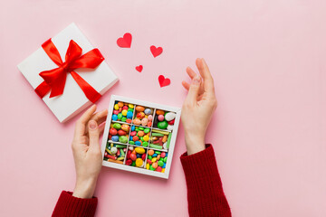 Female hands with delicious candies in box on color background