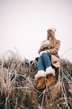 Unrecognizable woman in warm ugg boots holding cup of tea enjoying winter frozen nature