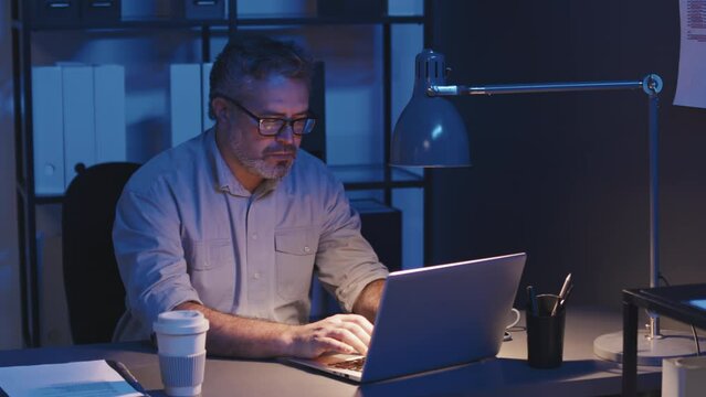 Medium Shot Of Serious Mature Businessman Concentrating On His Online Work On Laptop While Working Late At Night