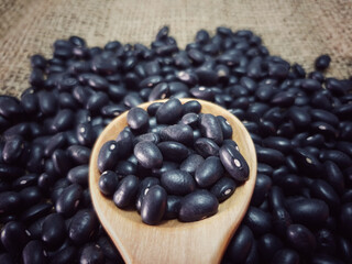 Black beans on wooden spoon isolated on sackcloth background. raw beans and organic superfood