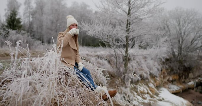 Young pretty woman holding cup of tea enjoying winter frozen nature by the sea