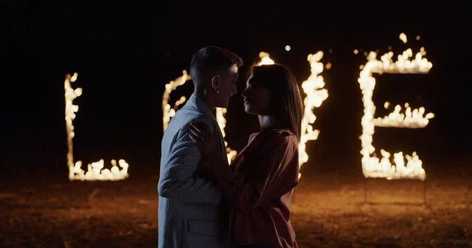Portrait of Young Homosexual Gay Female Couple kissing With the background of the Word LOVE composed of glowing sparkling pyrotechnic fire flame letters. Lesbian Lovers Celebrating their Relationship 