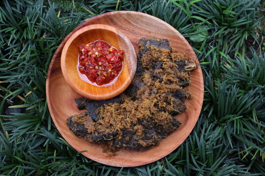 Fried Cow Lungs Gepuk, commonly called in Indonesia 'Paru Goreng Gepuk', Indonesian Traditional Food from Padang, West Sumatera. with chilli sauce on a wooden plate and on the grass, Top View