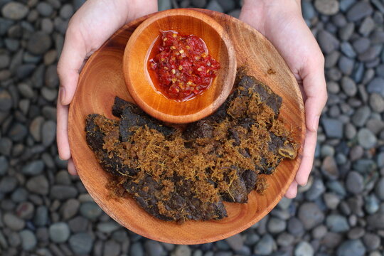 Fried Cow Lungs Gepuk, commonly called in Indonesia 'Paru Goreng Gepuk', Indonesian Traditional Food from Padang, West Sumatera. with chilli sauce on a wooden plate held by hands and on rock, Top View