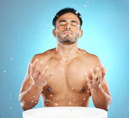 Facial, skincare and man in studio for water splash, wellness and grooming on blue background. Cleaning, beauty and moisture by Mexican model relax with luxury, routine and facial wash while isolated