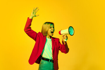 Excited young girl shouting in megaphone isolated over bright yellow background. Concept of news, human rights, youth, facial expression, emotions, active lifestyle.