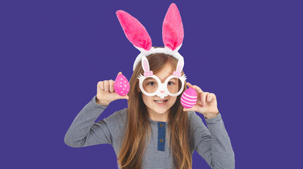 Cute little child wearing bunny ears on Easter day. Girl with painted eggs on bright violet background.