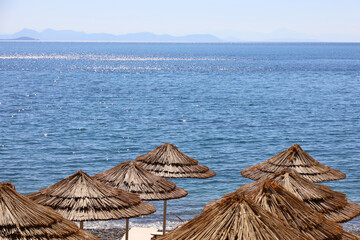 Empty beach with wicker parasols and deck chairs. Picturesque view to blue sea and mountains in mist, luxury resort