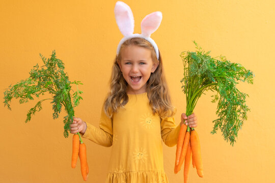 Yellow bright. Easter bunny rabbit ear. Excited surprise child girl holds big bunch of carrots isolated orange background. Healthy food and vegetables. Shopping