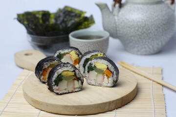 Five servings of homemade Korean Roll Gimbap (Kimbap) making a circle, surrounding the sauce and mayonnaise on a cutting board plus a pair of chopsticks and a cup of tea. Selective Focus