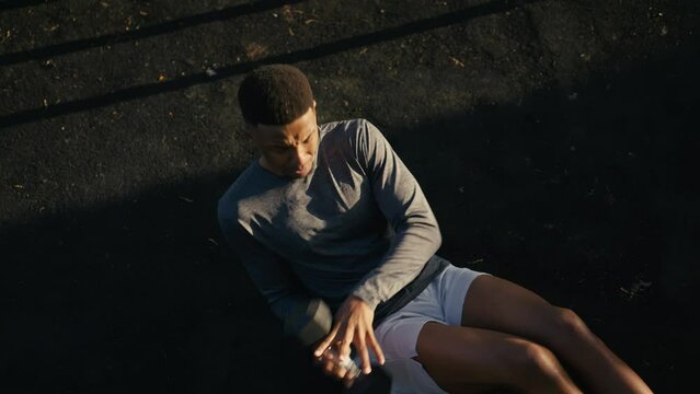 High angle view of young black man doing russian twist exercise with weights in park