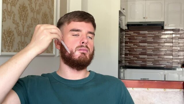 Young handsome man using beard growth product applying serum with dropper on face. Facial hair growth 