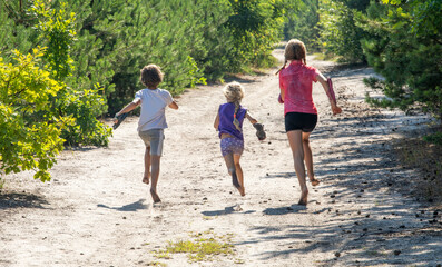 happy children run barefoot in the forest against the sun, horizontal.