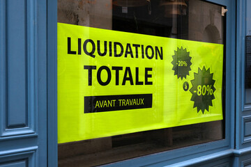 Affiche jaune collée sur une vitrine de magasin sur laquelle est écrit liquidation totale avant...