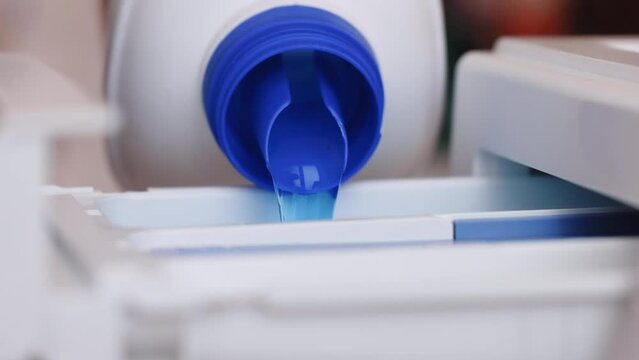 Woman pours necessary amount of liquid laundry detergent into compartment of washing machine from big bottle. Household chores concept.