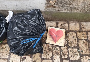 Sacs poubelles et pendule représentant un cœur par terre dans la rue, déchets ménagers sortis...