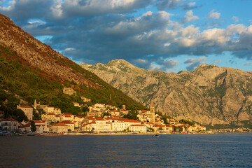 Fototapeta na wymiar Seaside town in the rays of the setting sun against the backdrop of majestic mountains. Bay of Kotor, Montenegro