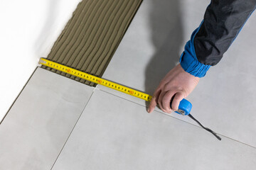 Tiler worker placing or tiling gray ceramic tile in the position over adhesive glue with lash tile leveling system, renovation or recontruction, concept of building