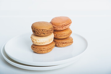 Stack of delicious freshly baked caramel, coffee and vanilla flavoured macaron confections on white plate against white background. Copy space. French sweet food speciality.