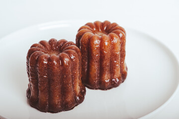 Delicious freshly baked canele, rum and vanilla flavored french pastry with caramelized crust on white plate against white background, close up. A specialty of the Bordeaux region of France.