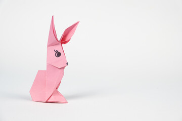 A pink origami rabbit on a white background. Crafts for Easter, fold from paper, do it yourself, place for text.