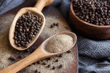 Heap of black pepper, peppercorns in spoon with milled powder on rustic background, dried spice peppercorn concept