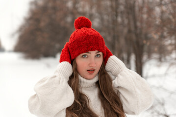 Portrait of blue-eyed girl in fashionable knitted red hat and mittens and woolen sweater in winter forest. Ladies knitwear