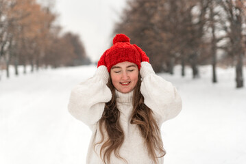 Laughing happy girl with closed eyes in red hat and mittens in winter park. Beautiful young woman on winter walking