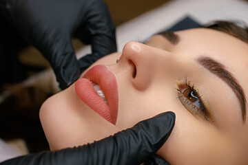Finished work on permanent lip makeup for a model, lips close-up, the master tightens the corners...