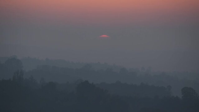 Setting sun above hill layers in fog, big bright setting sun