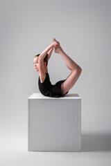 A flexible sports girl gymnast in a black gymnastic bodysuit performs a workout with the help of a cube. Stretching exercises with a cube