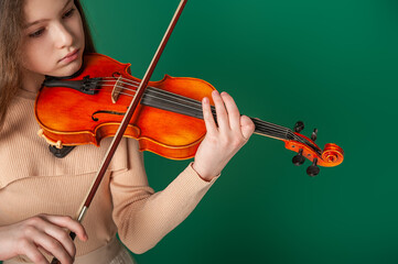 A girl in beige clothes plays the violin on a plain green background. Close-up
