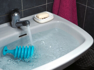 Sink in the bathroom full of water and a blue plunger.