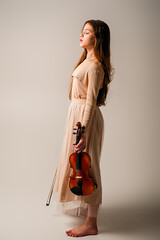 A girl in a long beige skirt plays the violin on a beige background.