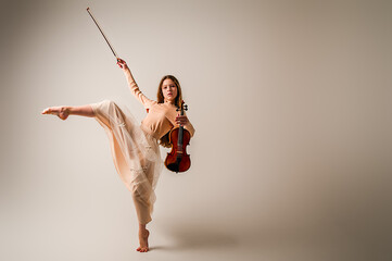 A girl in a long beige skirt plays the violin on a beige background.