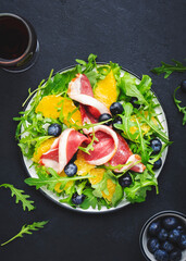 Delicious salad with smoked duck, oranges, blueberries, arugula and lettuce with red wine, black table background, top view