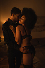 seductive african american woman in sexy lingerie embracing with young boyfriend at home at night
