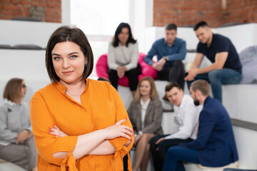 a brunette woman in an orange blouse with men and women in the office.