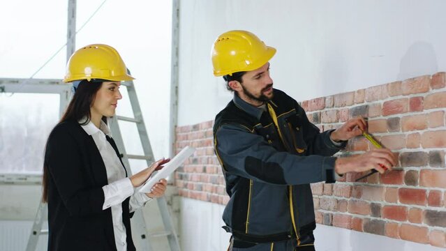 Construction site charismatic woman in a suit with safety helmet supervisor make a verification of reparations together with the constructor worker they wearing safety helmets