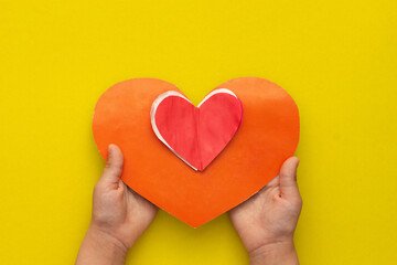 Flat lay of child hands holding diy red heart as gift for Valentine day on yellow background