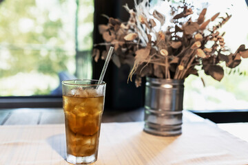 Beautiful still life with dried flowers in a tin vase and a long Island cocktail on the table by the window