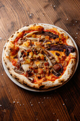The top view of delicious Italian untypical gourmet vegetarian pizza with mozzarella, pumpkin, walnuts, red radicchio on the wooden background 