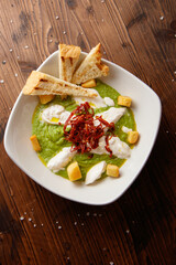 Top view of delicious appetizer Mexican avocado sauce guacamole with burrata, red chili pepper and grilled bread on wooden background 