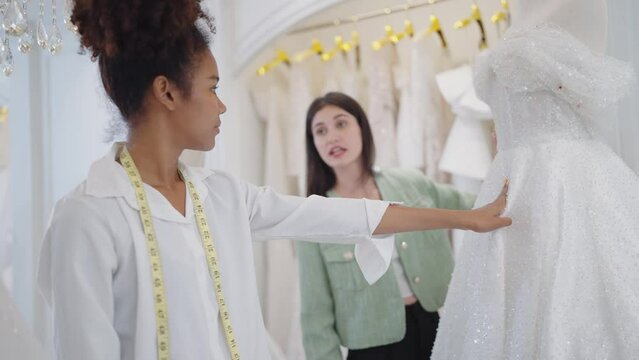 Two professional woman fashion designer talking and brainstom for designing a white bridal gown at wedding studio 
