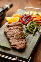 Top view of ribeye well done steak on the stone modern dish with rosemary, green beans, lemon, carrots, zucchini 