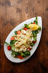 top view of italian delicious salad with shrimps, cherry tomato, lemon, valerian grass, rucola in white plate on the wooden background 