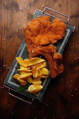 top view of schnitzel with potato cheeps on the stone dish at the wooden background; fast food 